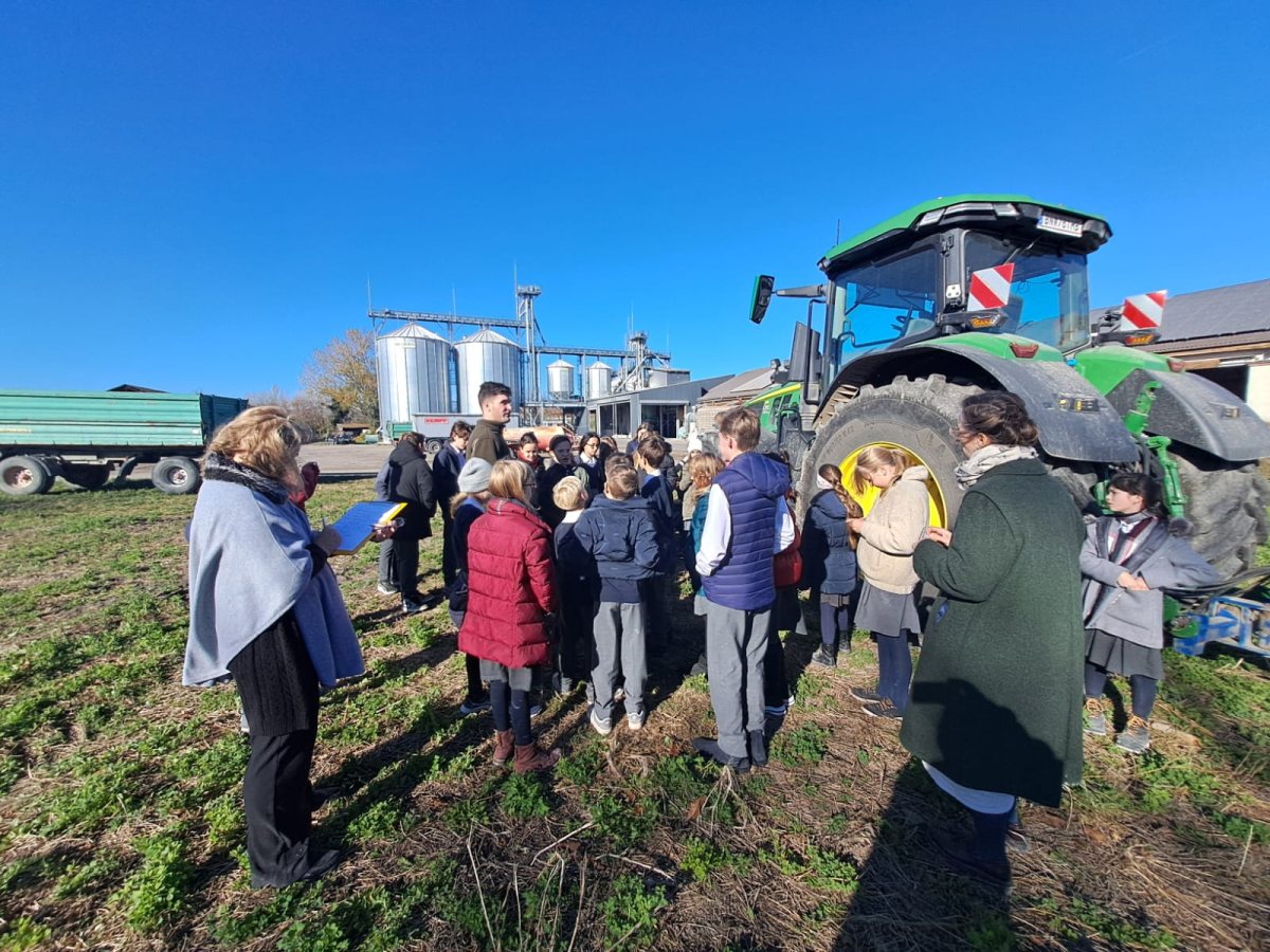 Klassen beim Rundgang am Bio-Hof neben einem großen Traktor