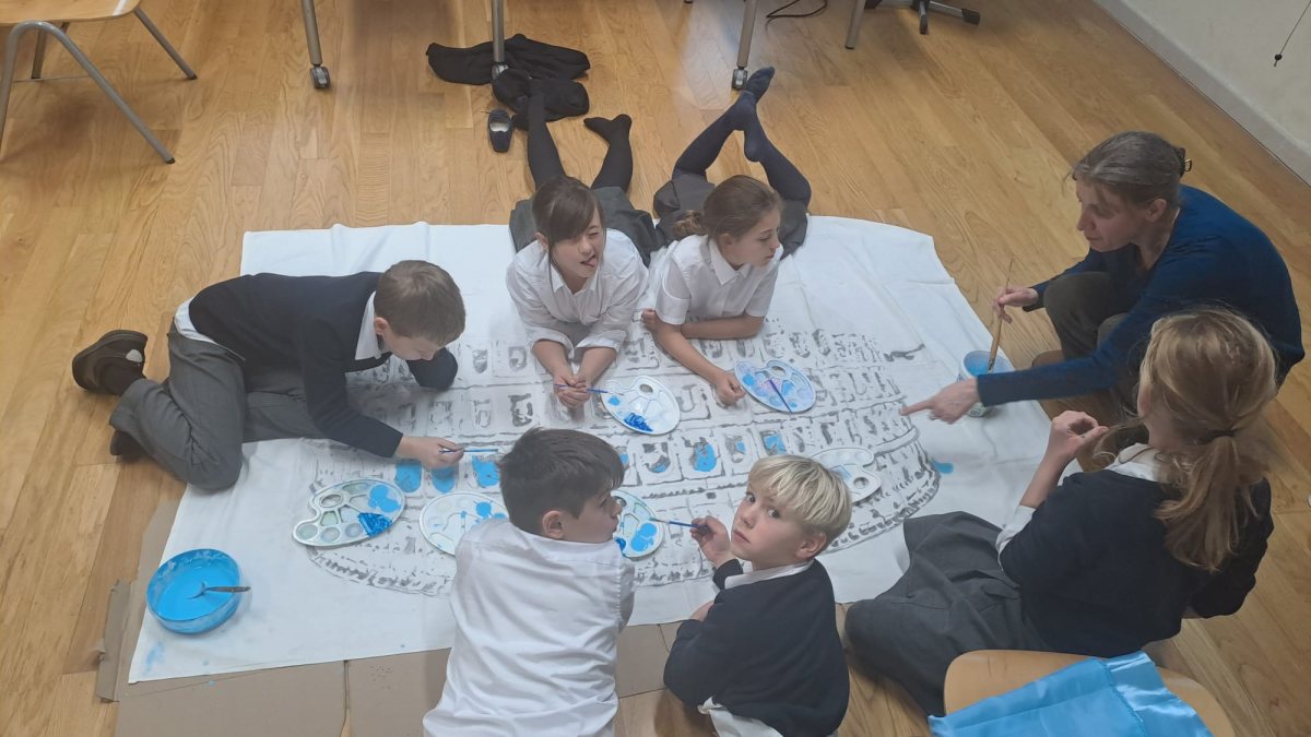 Kinder der 1. Klasse malen auf dem Boden an einem großen Bühnenbild